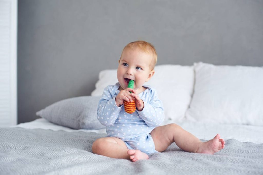 Cute baby boy playing with knitted toy on bed at home