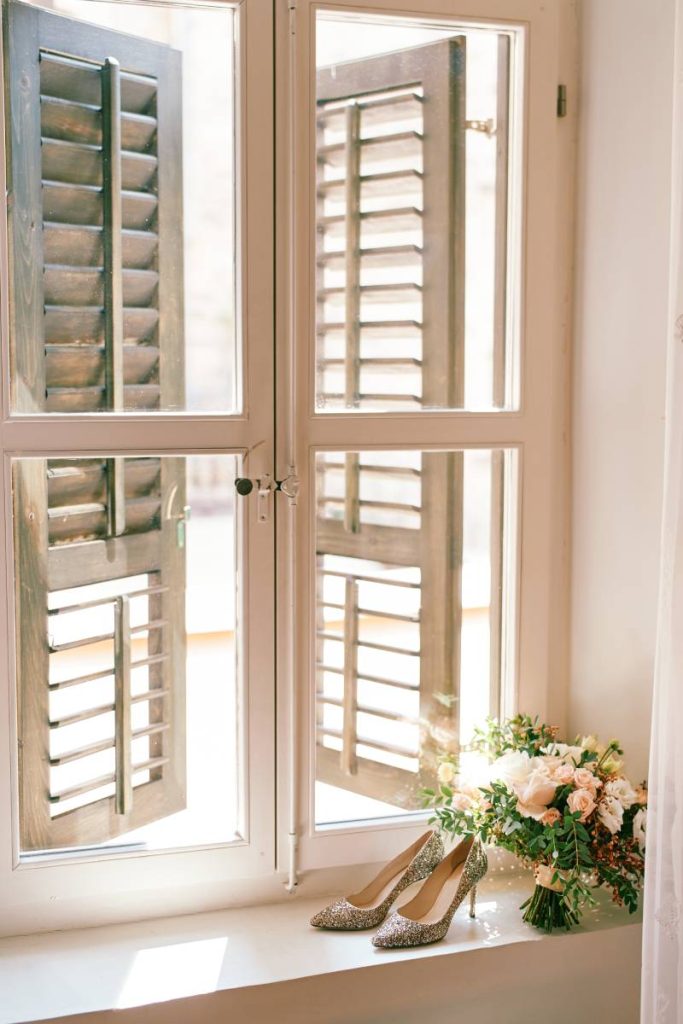 Bride shoes with a bouquet of flowers stand on the windowsill in the room. High quality photo