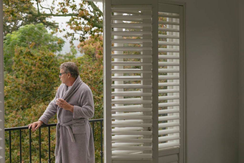 Side view of thoughtful active senior Caucasian man with coffee cup standing in balcony in a comfortable home