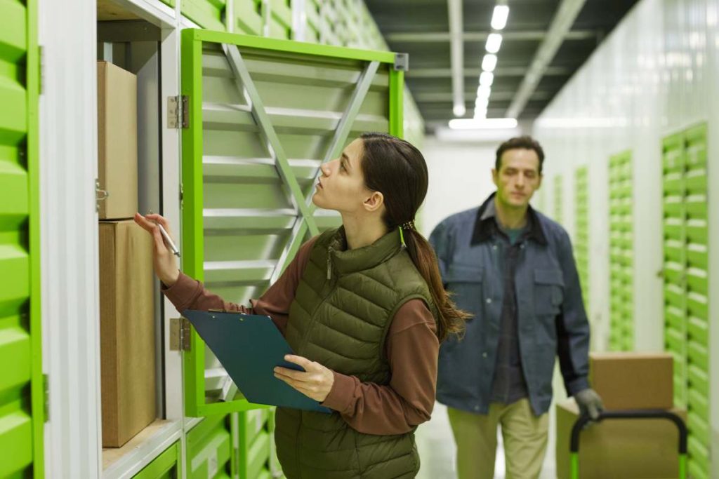 Young woman checking boxes with man carrying them in the background they working in warehouse