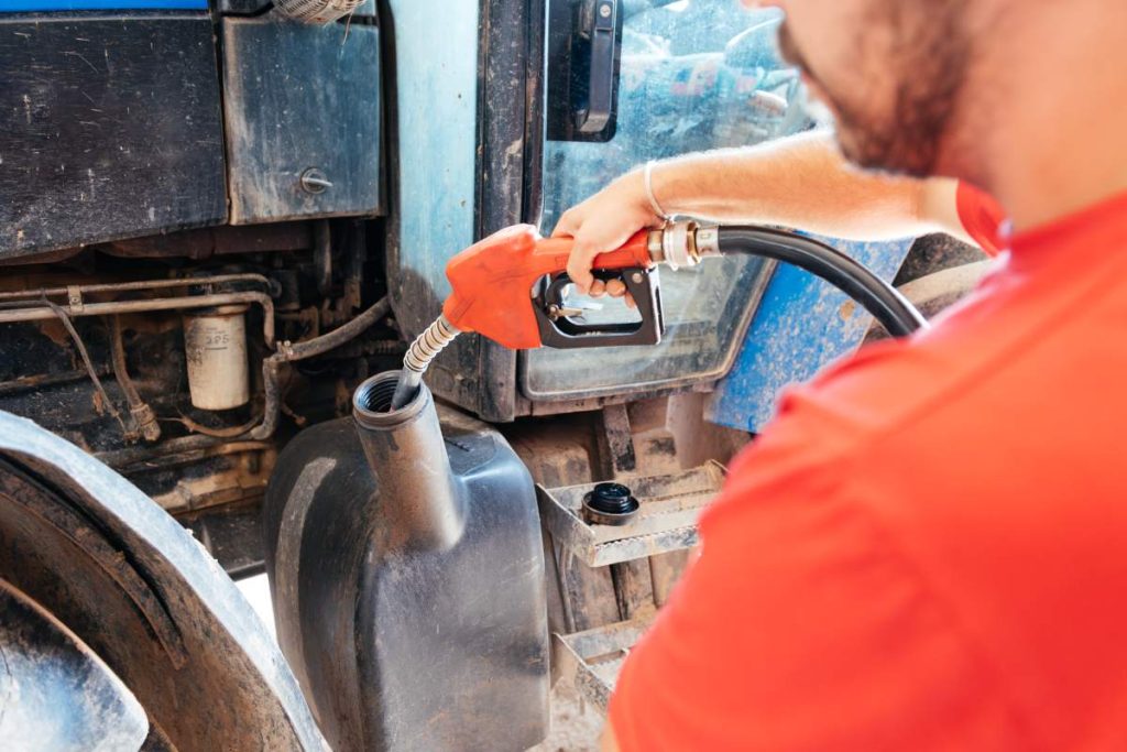 Close-up of a person holding a fuel nozzle, topping up a tractors tank; a farming activity essential for agricultural operations.