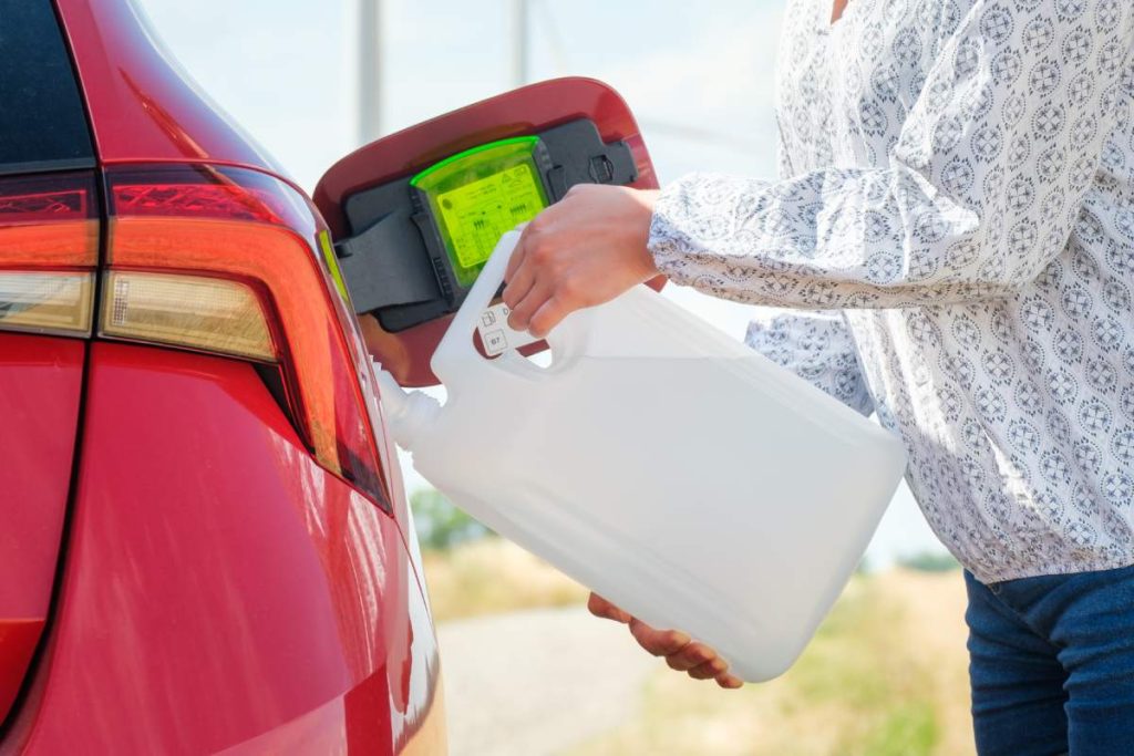 Close up woman refilling the red car with fuel or a diesel engine fluid from canister in the field