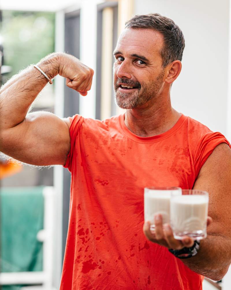 Portrait of a muscular man posing with nutritional supplement. He's showing his muscles while holding two drinks in another hand. Vertical shot