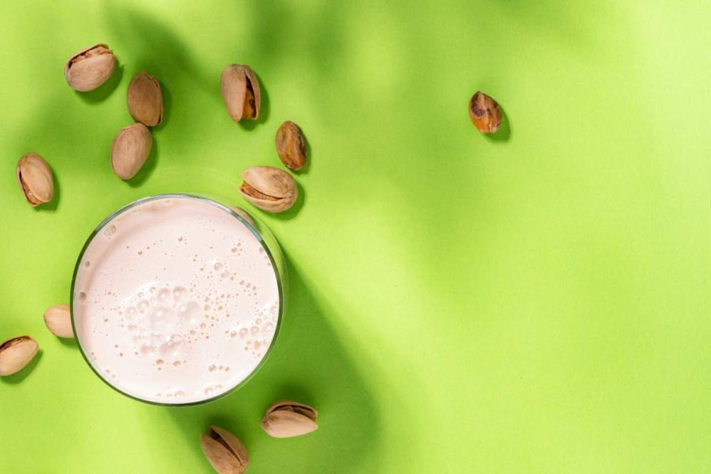 Vegan Pistachio nut milk in bottles, closeup, green background. Non dairy alternative milk. Healthy vegetarian food and drink concept. Copy space, top view