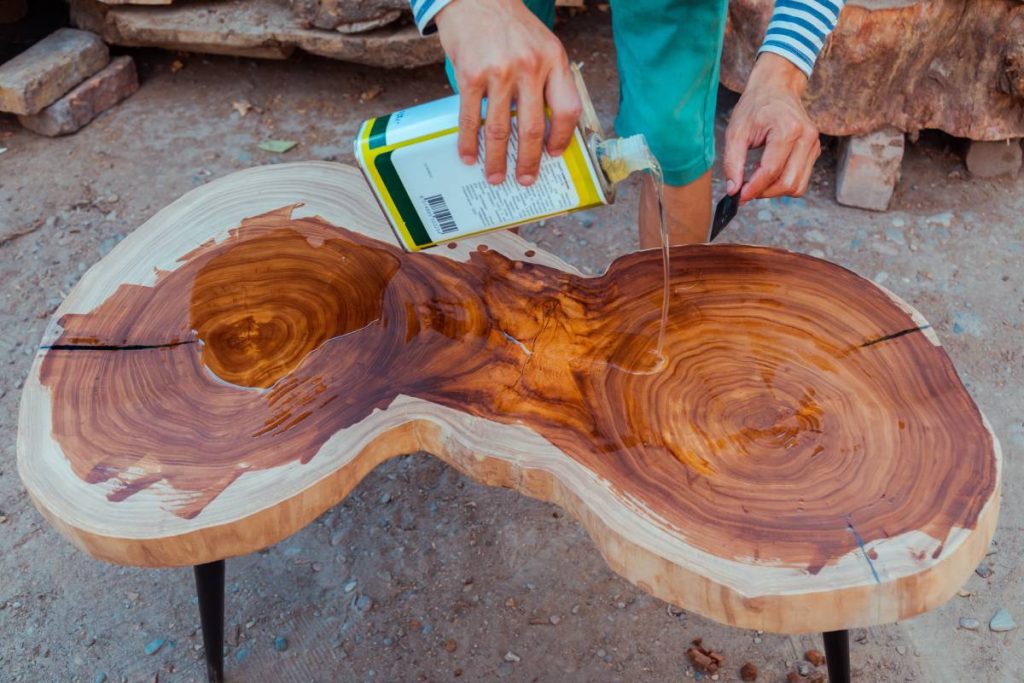 Carpenter pouring linseed oil on a wooden table. Process of making wood table